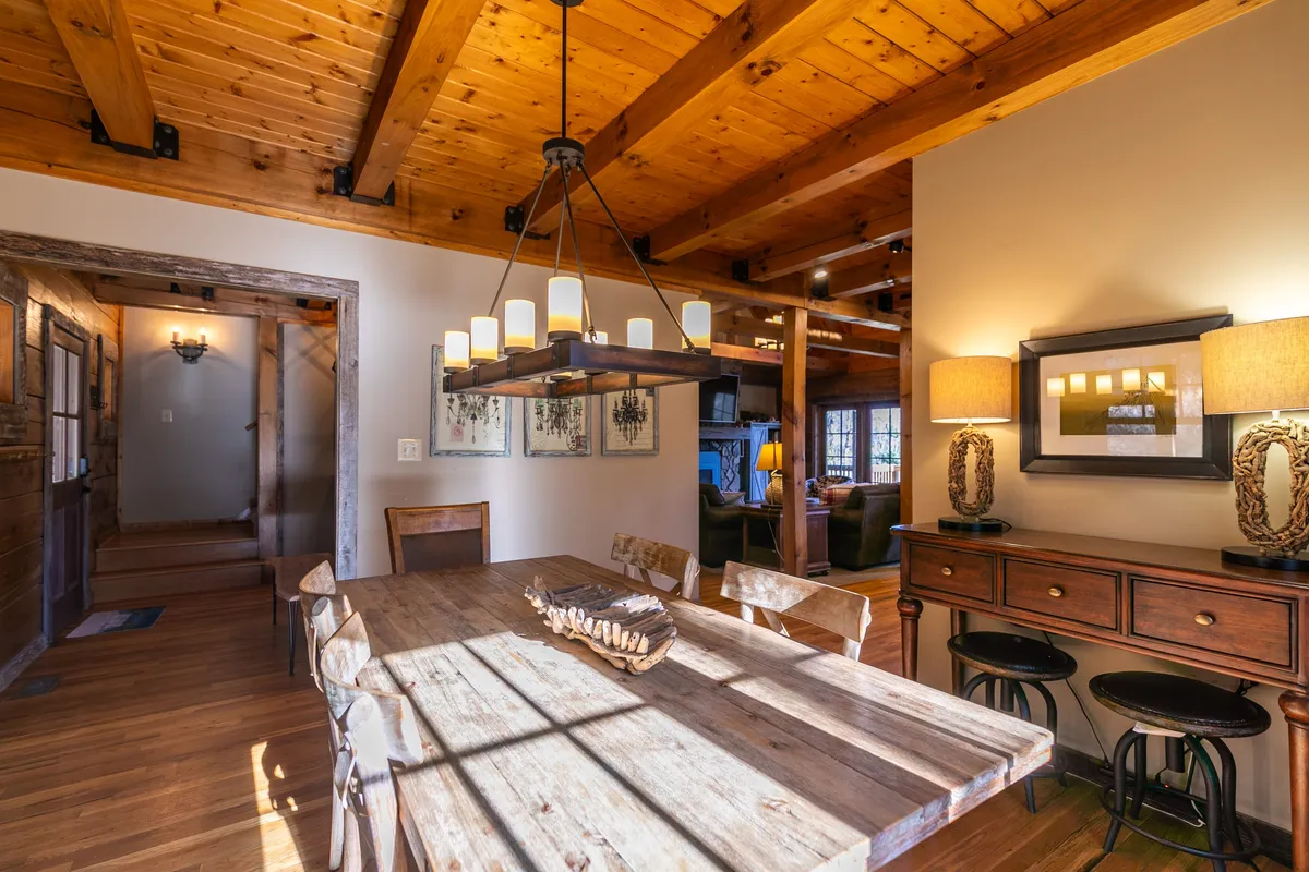 A large wooden dining table set under a decorative chandelier with candles, flanked by wall art and a console table with lamps. The setting suggests warmth and togetherness, offering a space for shared meals and game nights after days spent exploring the High Country.