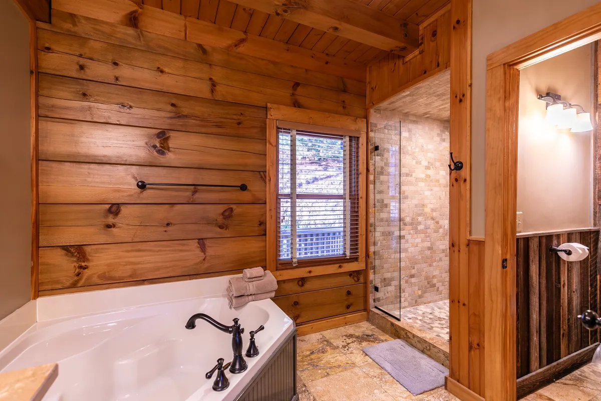 This bathroom features a luxurious jacuzzi tub, a glass-enclosed shower, warm wooden walls, and a window that allows plenty of natural light to filter in. The spa-like elements create a calming atmosphere perfect for relaxation and rejuvenation.