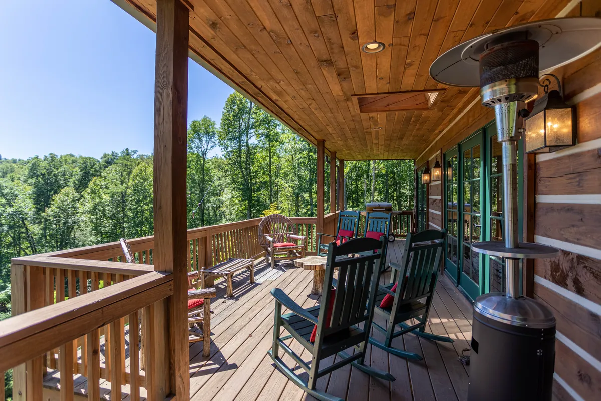 A peaceful wooden deck outfitted with rocking chairs and surrounded by a lush forest. A patio heater suggests comfort on cooler days, while the open setting invites socializing, sunrise coffee, or evening relaxation.