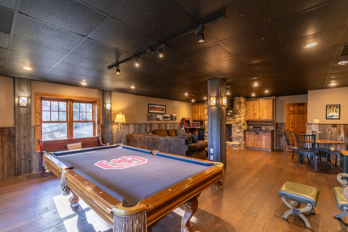 A cozy entertainment space featuring a pool table, comfortable seating area, and a stone fireplace. The arrangement is inviting and conducive to friendly games, intimate conversations, and relaxed evenings.