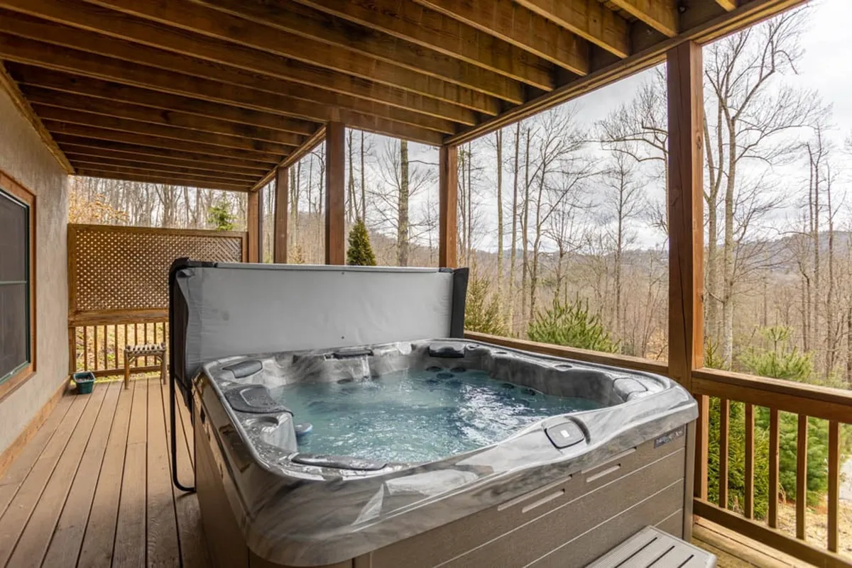 An inviting hot tub sits on a wooden deck surrounded by tall trees, offering a private yet open setting for relaxation, stargazing, and soaking in mountain views. The tranquil atmosphere highlights the connection to nature and year-round enjoyment of the outdoors.
